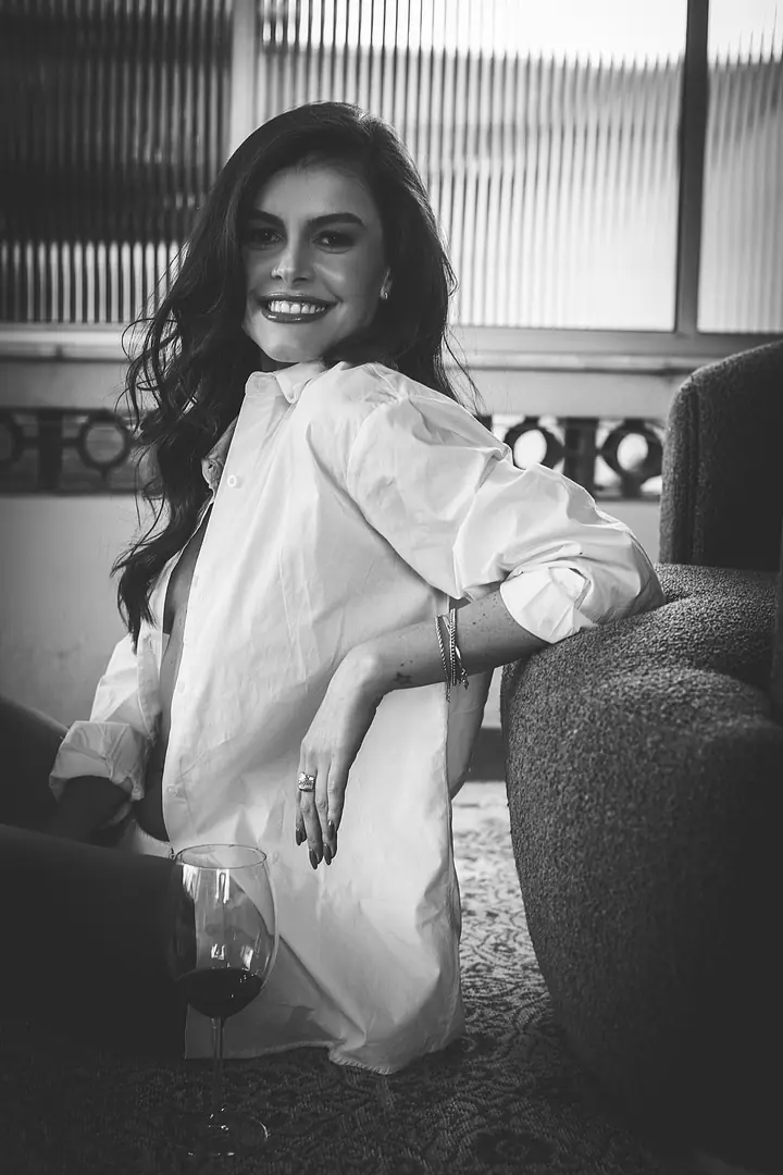 Mulher de camisa branca sentada no chão encostada em poltrona, preto e branco