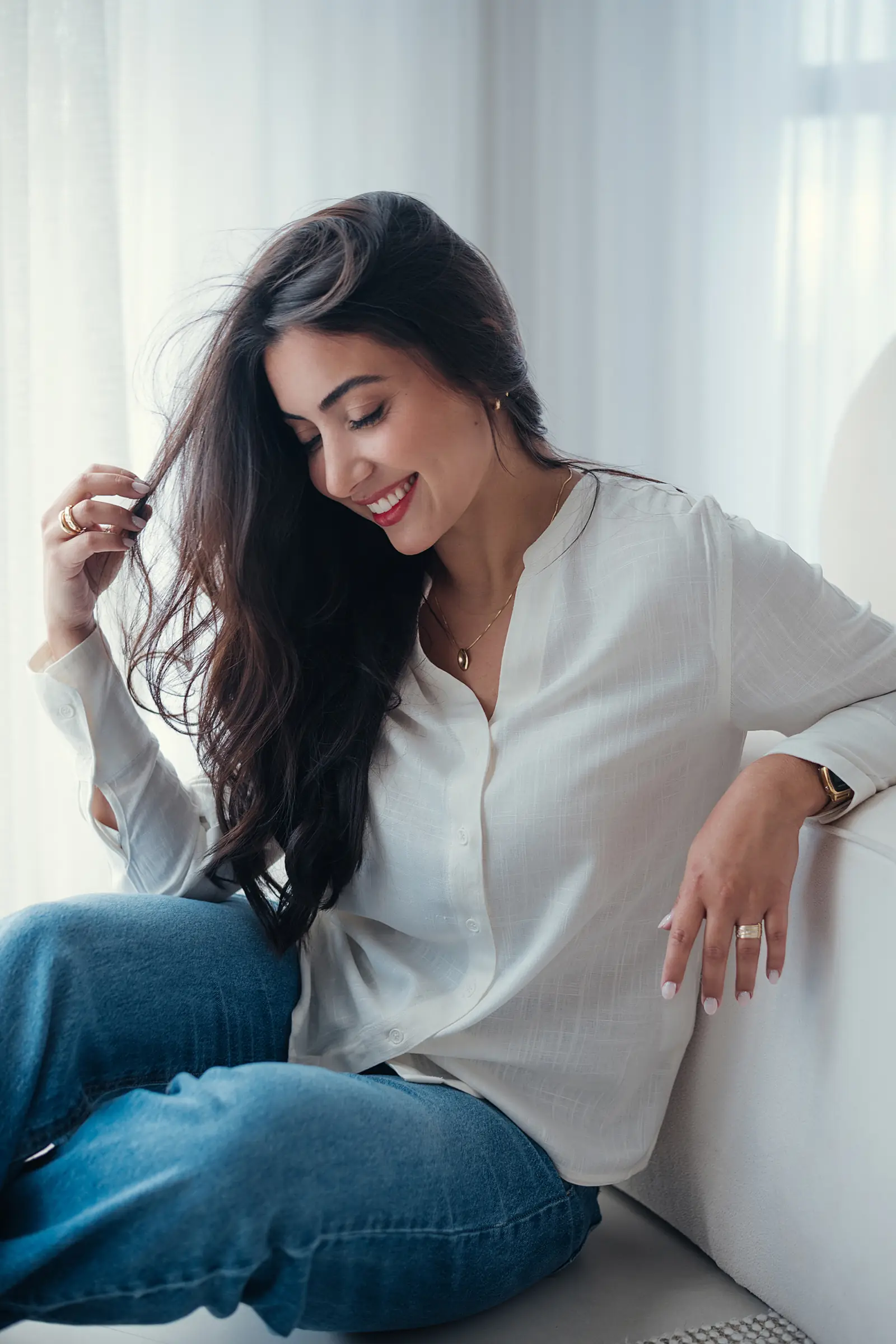 Mulher de camisa branca e calça jeans olhando para baixo, ambiente claro