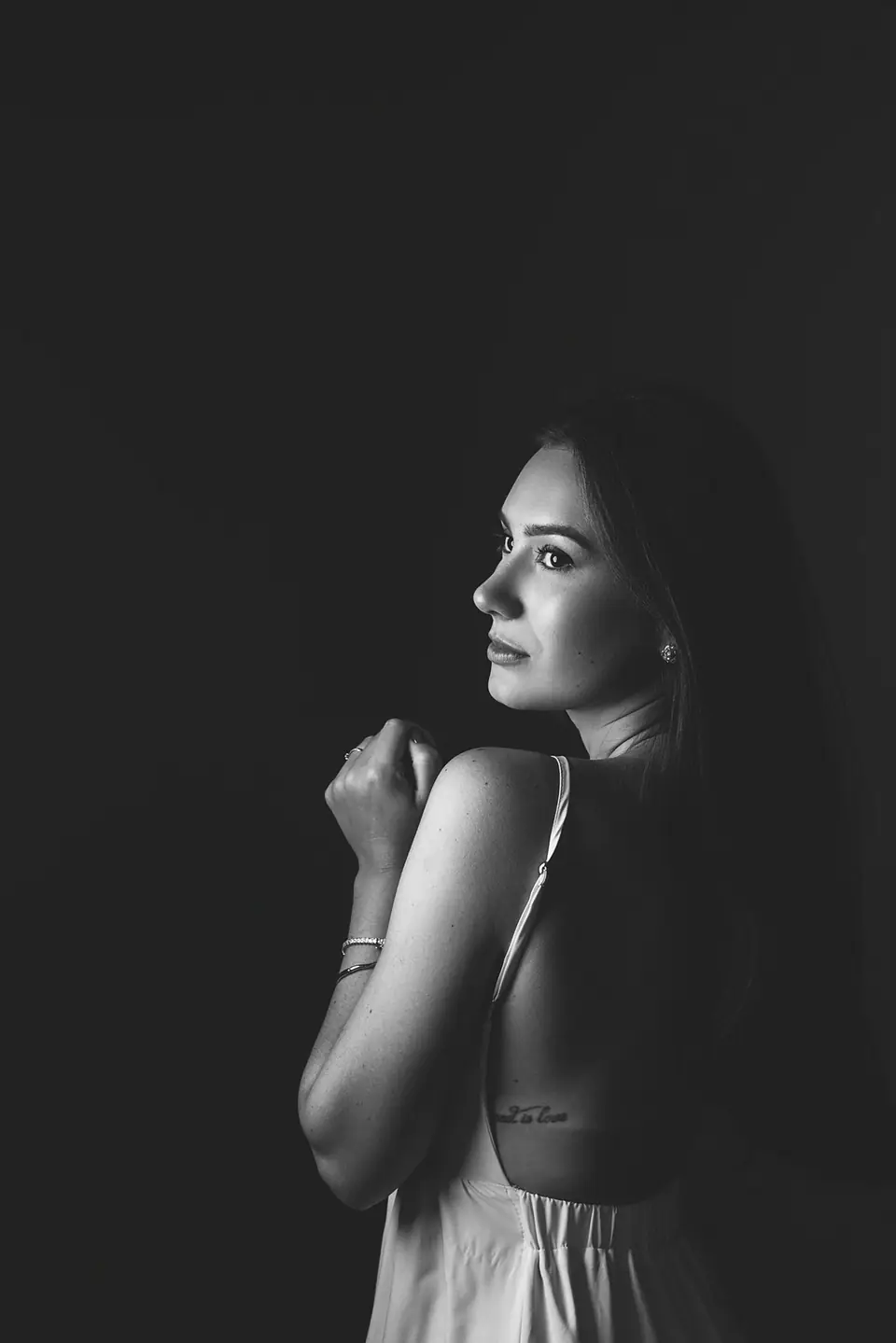 Perfil de mulher de alça fina sobre fundo escuro, braços cruzados