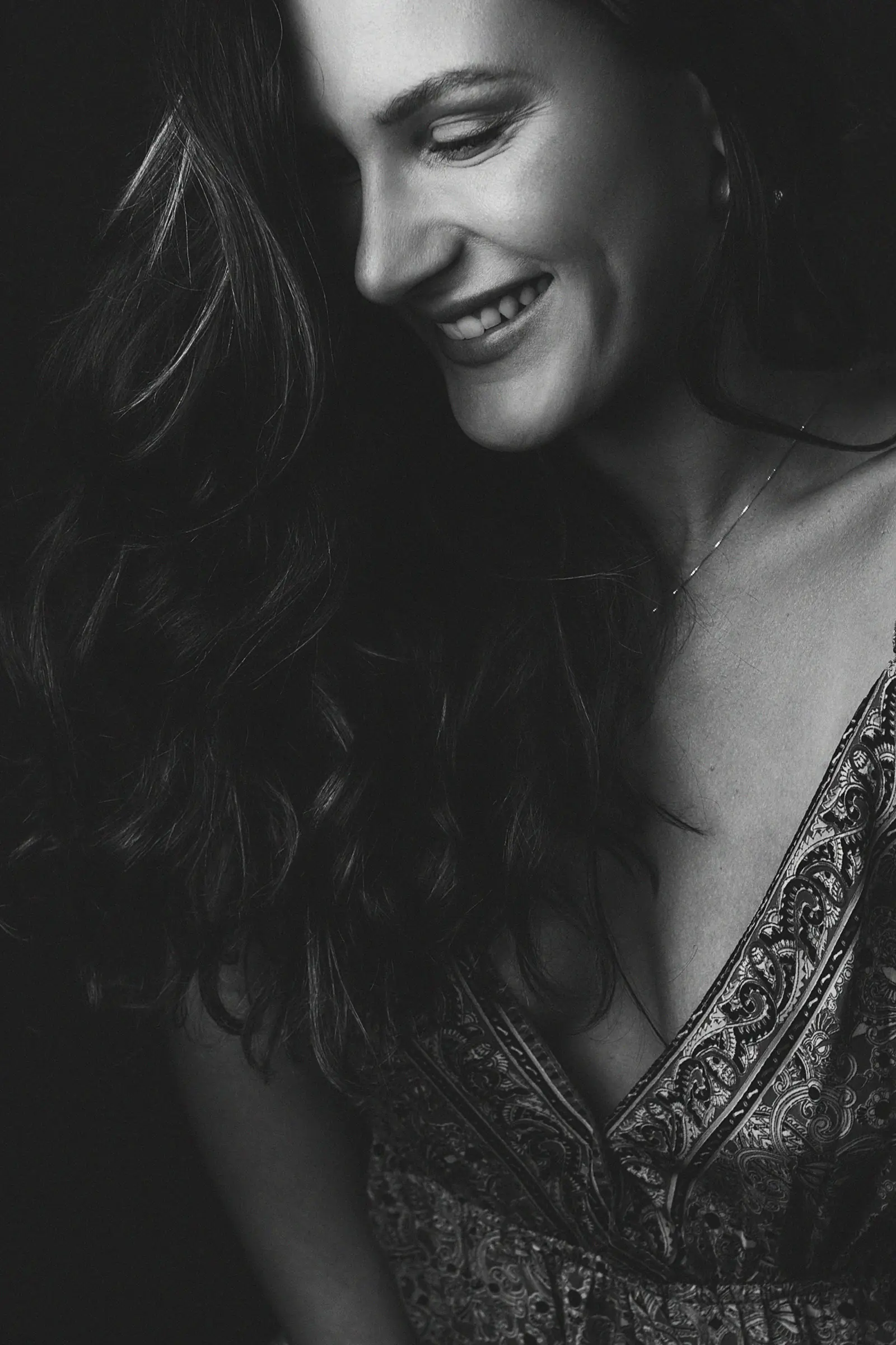 Sorriso de perto com colar fino, cabelo escuro solto, preto e branco