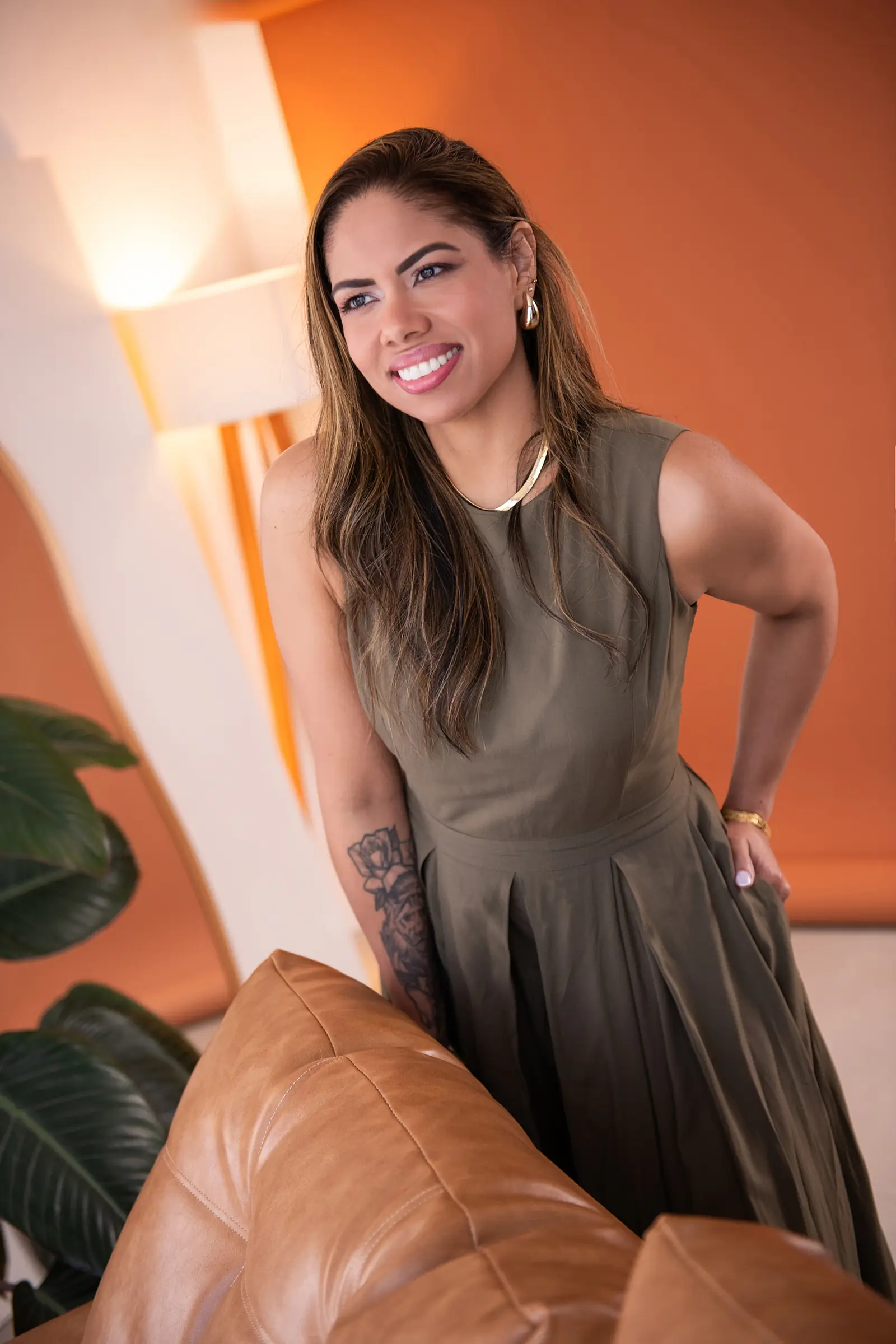 Mulher de vestido verde-oliva com a mão na cintura, luminária acesa ao fundo
