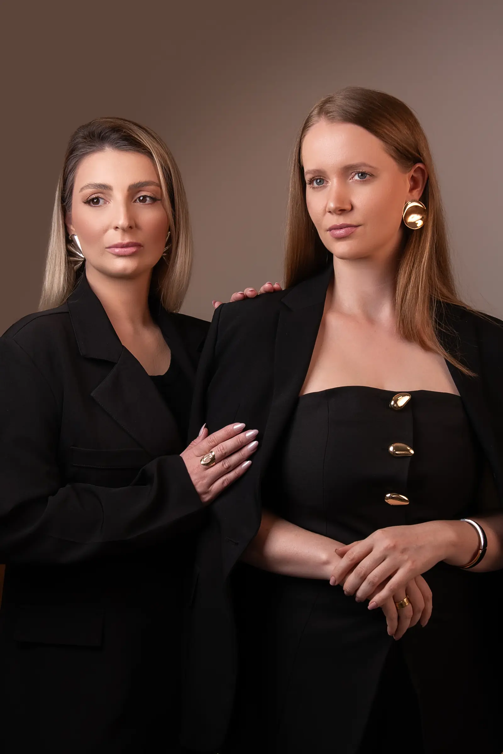Duas mulheres de preto lado a lado, uma com a mão no ombro da outra