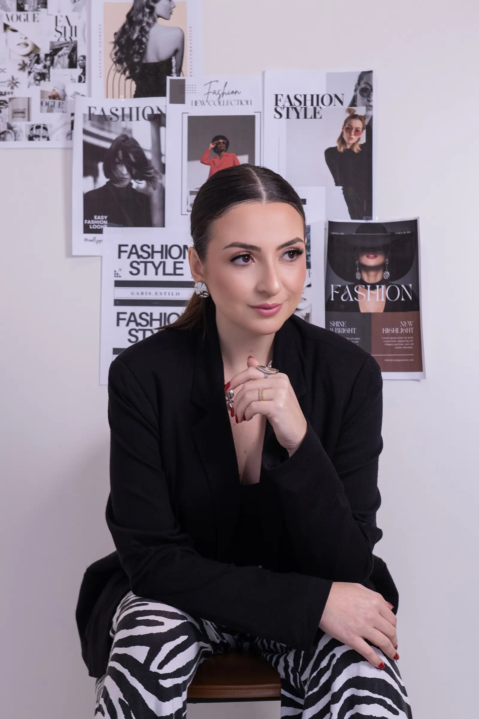 Mulher de blazer preto com as mãos unidas, revistas de moda na parede