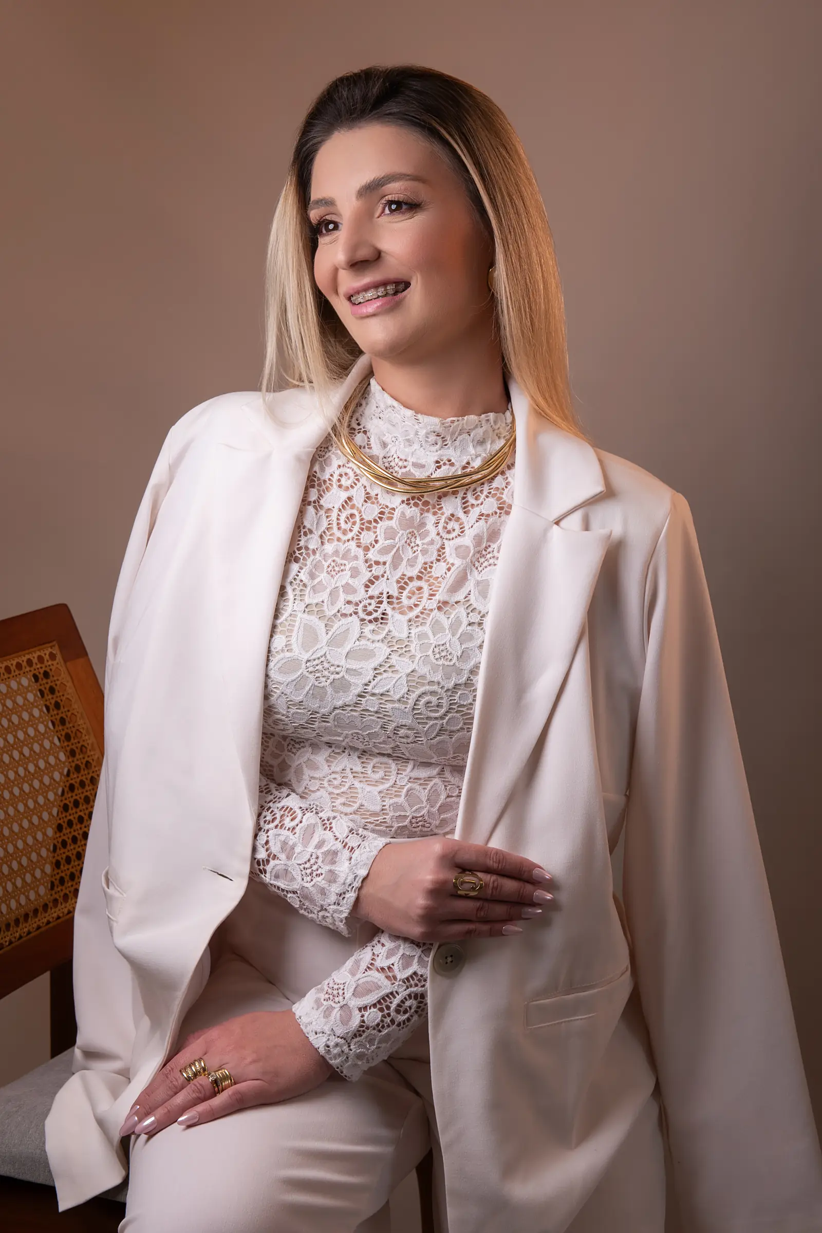 Mulher de blazer branco sobre blusa de renda, com colar dourado