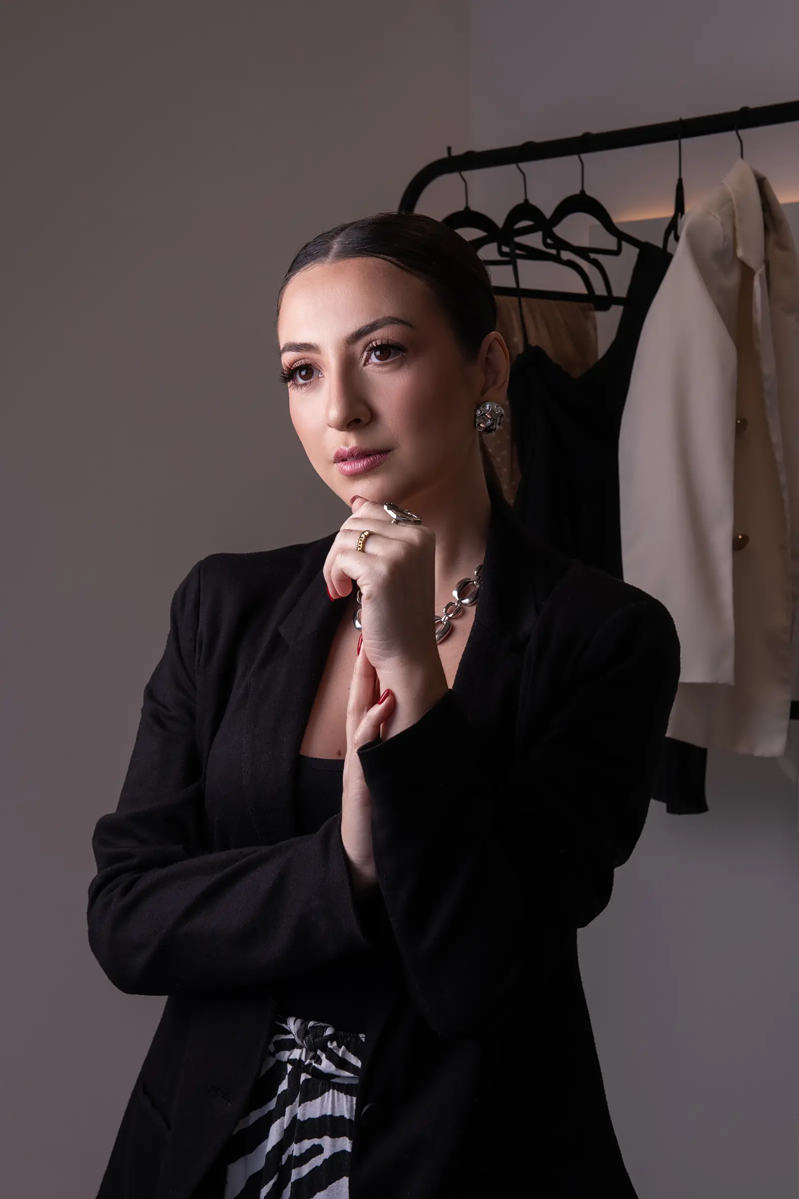 Mulher de blusa preta com as mãos unidas, arara de roupas ao fundo