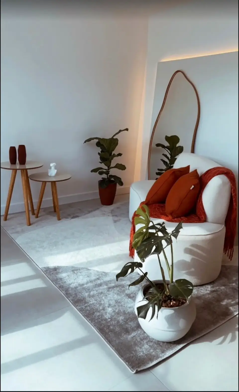 Cenário do estúdio com poltrona branca, almofadas terracota, espelho arqueado e plantas