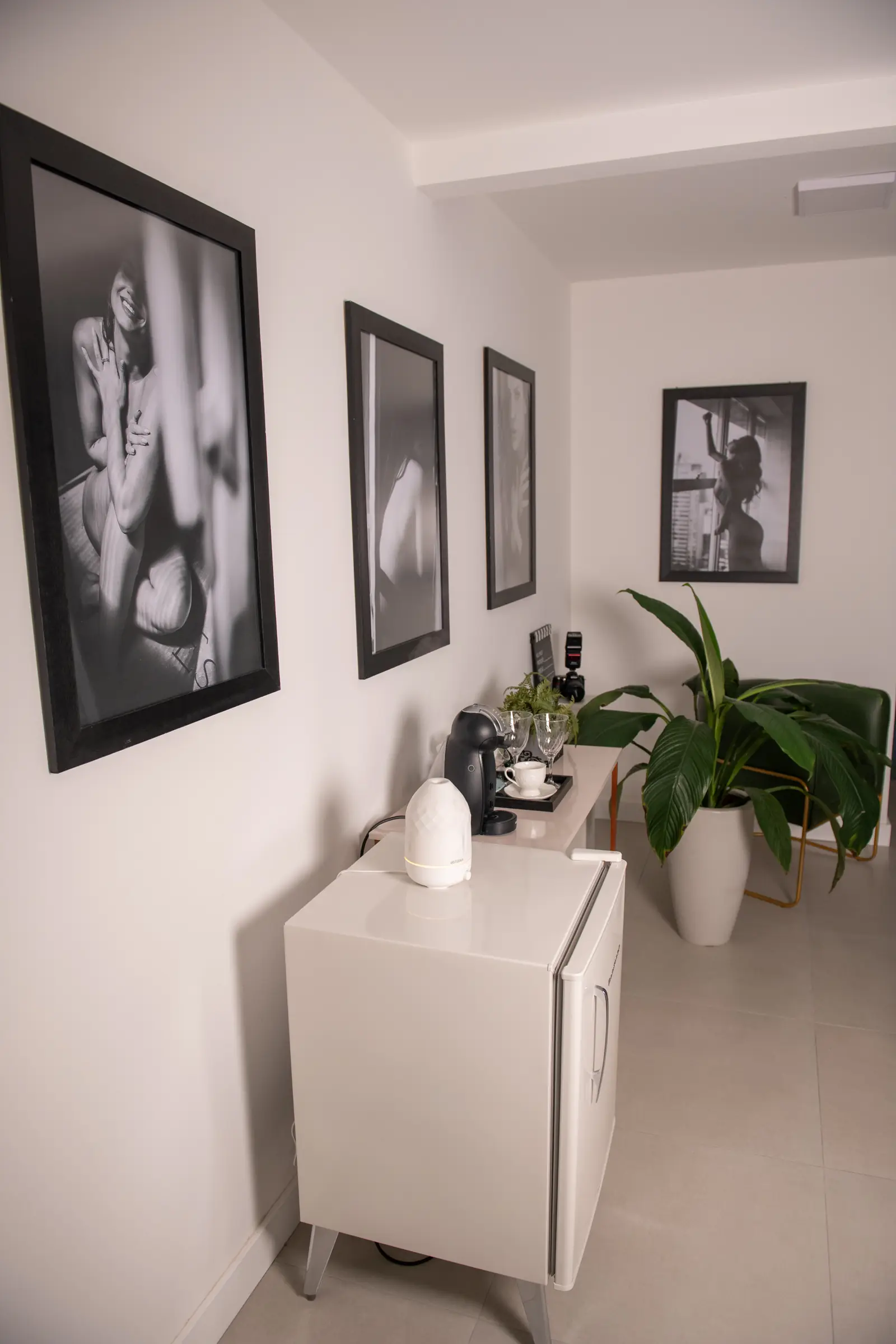Recepção do estúdio com quadros de retratos em preto e branco, cafeteira e plantas