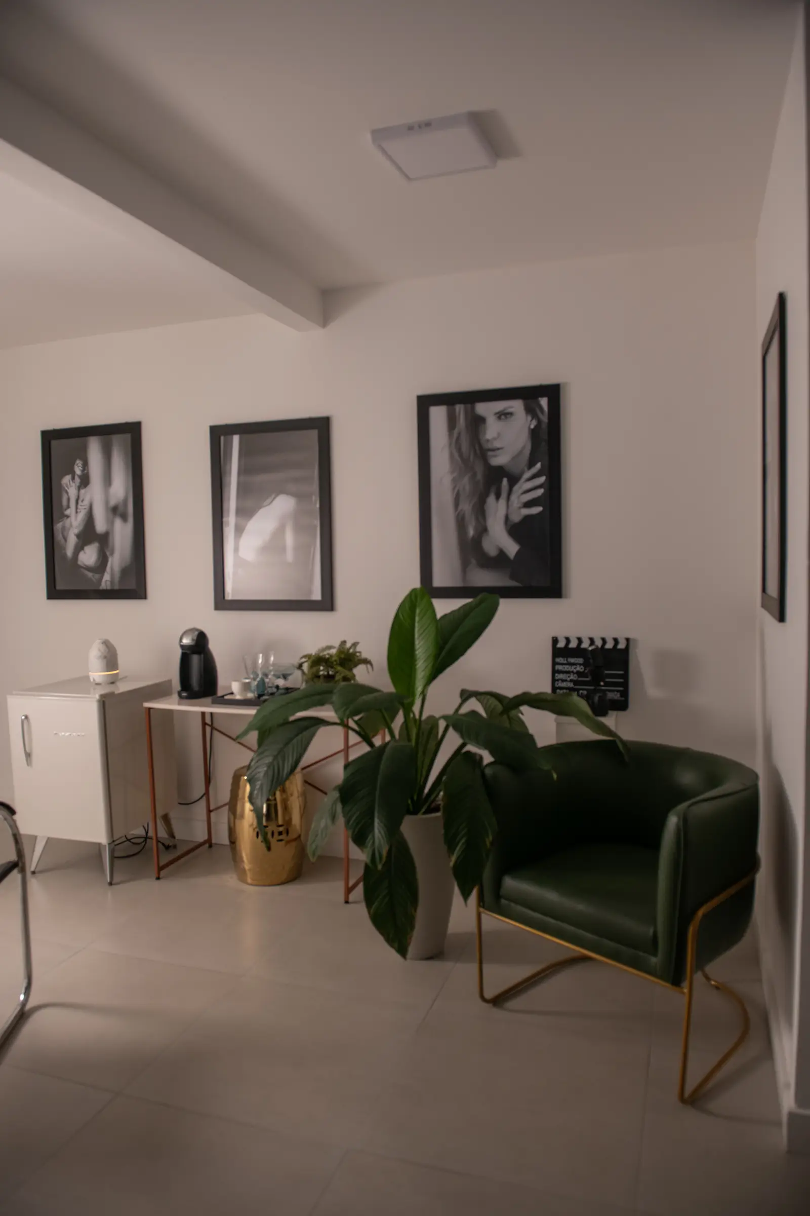 Sala de espera do estúdio com poltrona verde, quadros em preto e branco e cantinho do café
