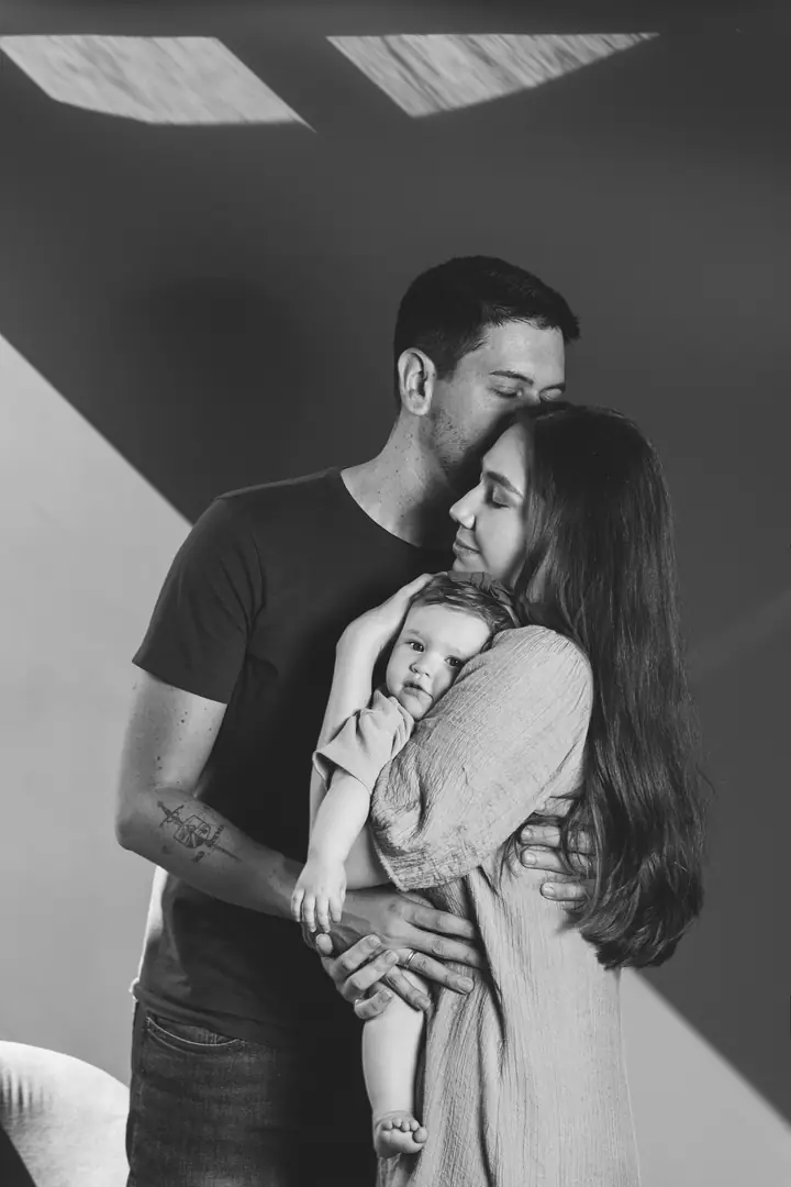 Casal abraçado segurando bebê recém-nascido, retrato em preto e branco