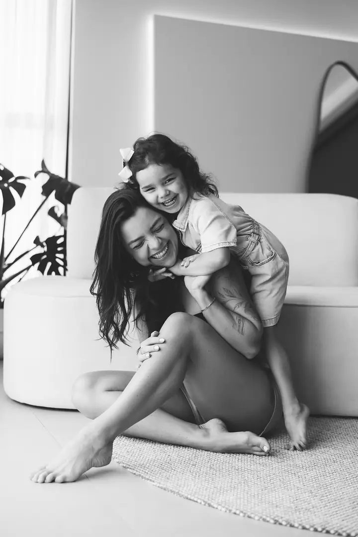 Mãe sentada no chão rindo com a filha pequena no colo, preto e branco