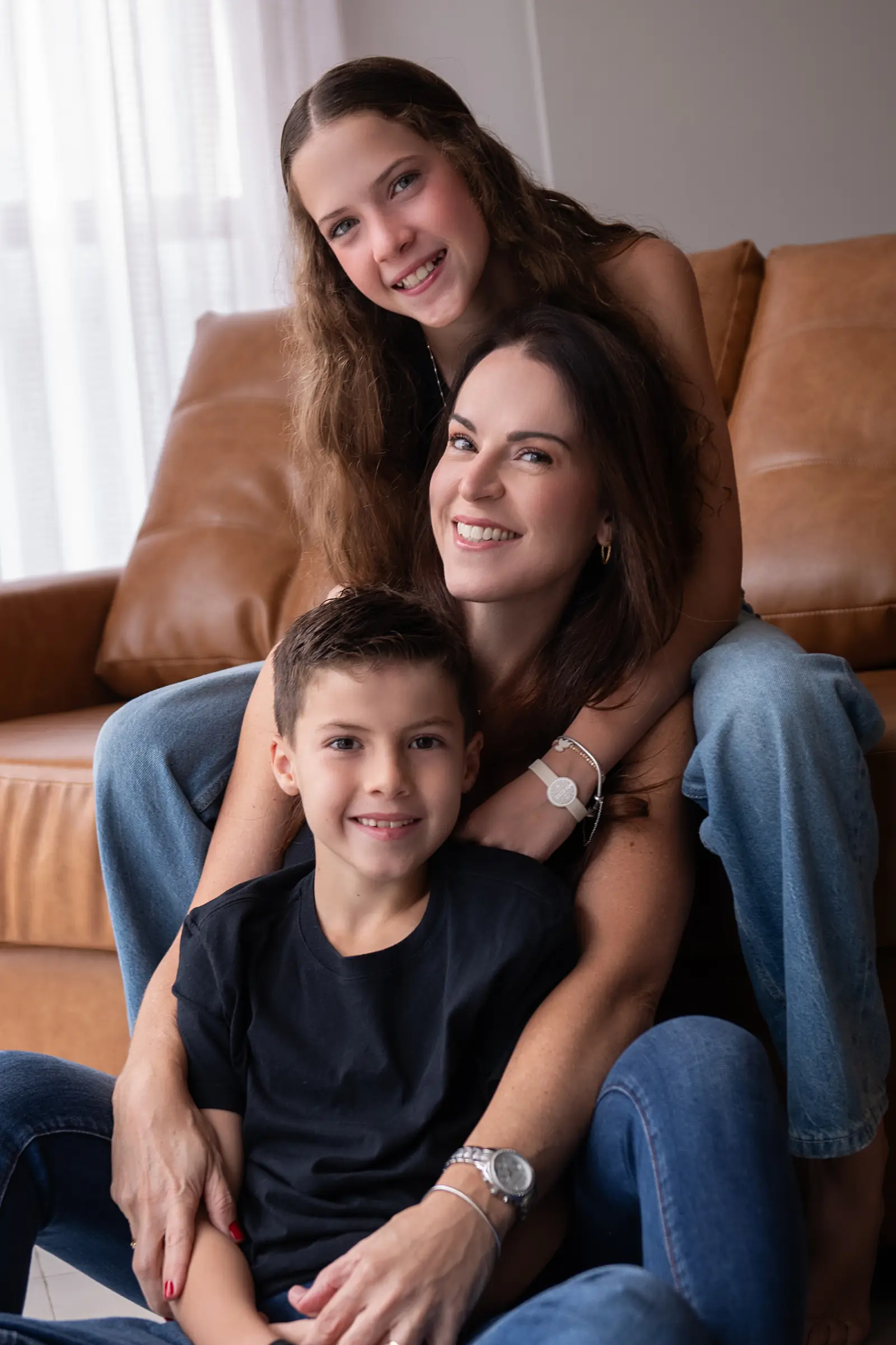 Mãe com os três filhos em sofá de couro, todos sorrindo