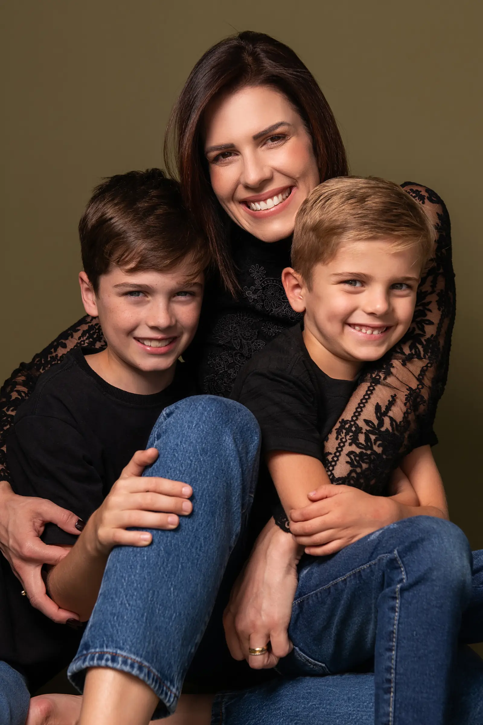 Mãe abraçada aos dois filhos meninos, fundo verde-escuro