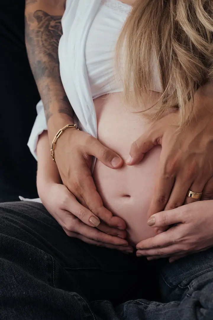 Mãos do casal formando um coração sobre a barriga da gestante