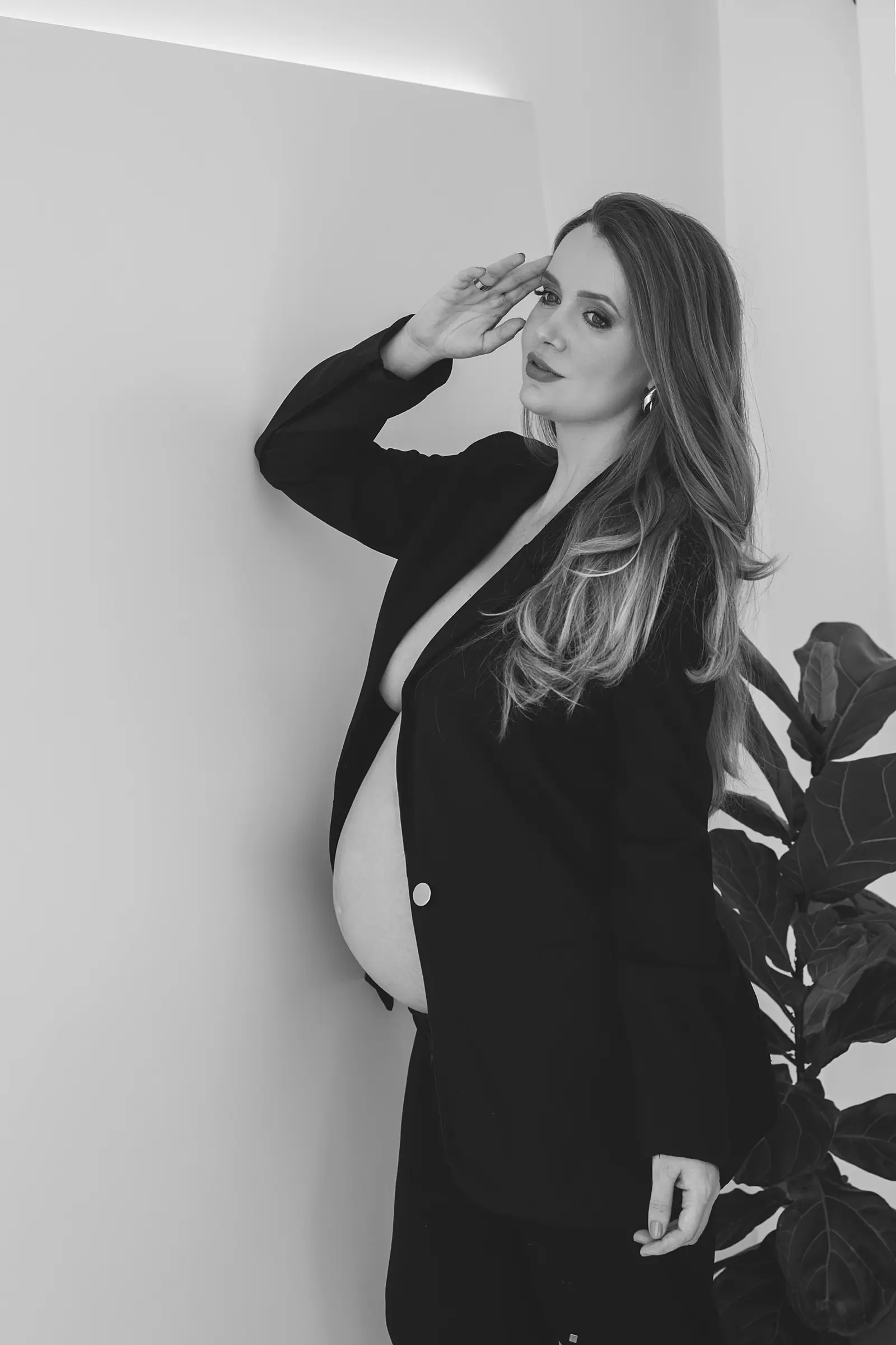 Gestante de blazer com a mão no rosto, fundo claro, preto e branco