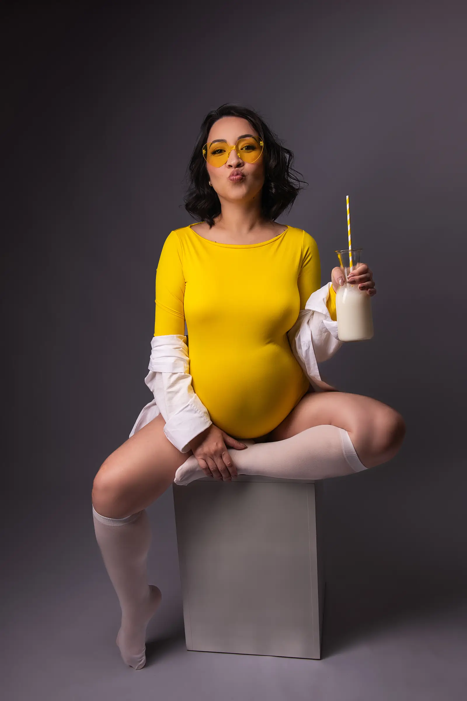 Gestante de body amarelo e camisa branca sentada com garrafa de leite e óculos
