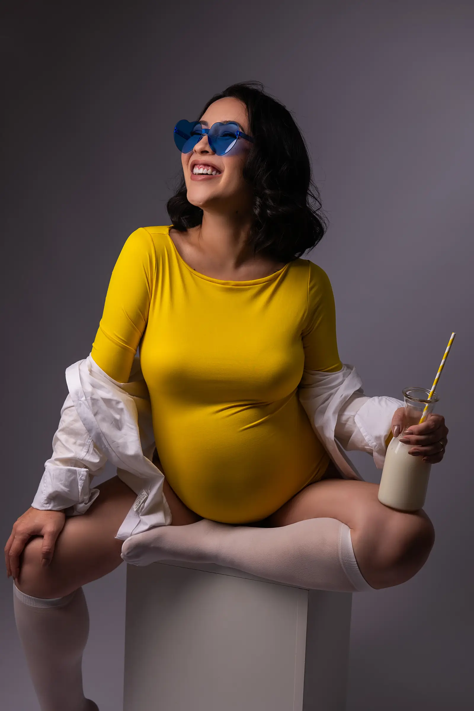 Gestante de body amarelo com óculos azul, sentada com garrafa de leite