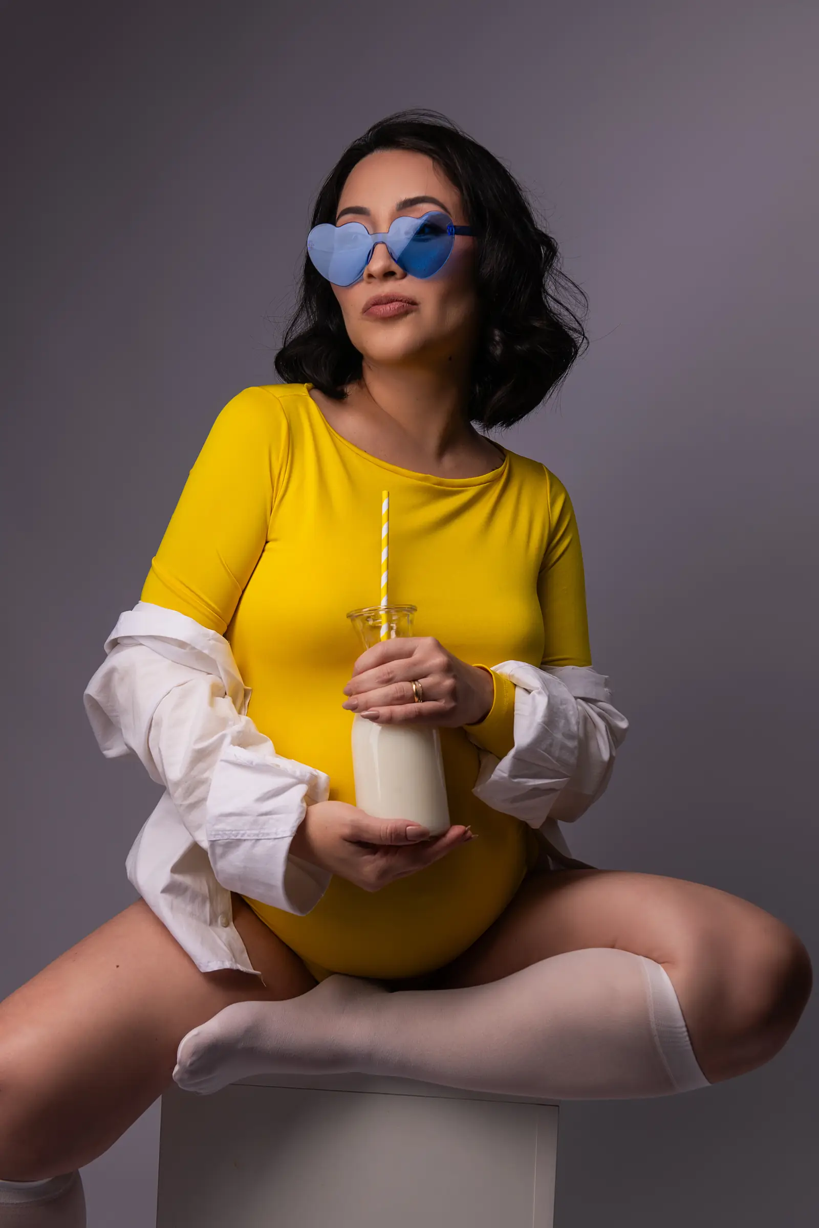 Gestante de body amarelo e óculos em formato de coração, garrafa na mão