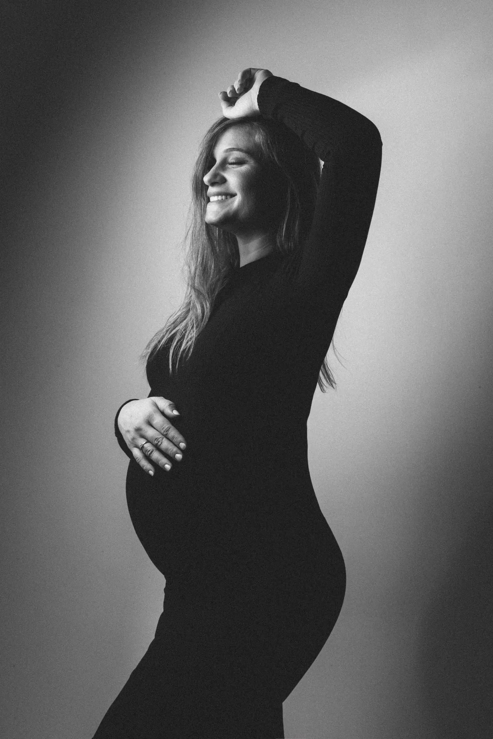 Perfil de gestante de vestido preto com a mão na barriga, preto e branco