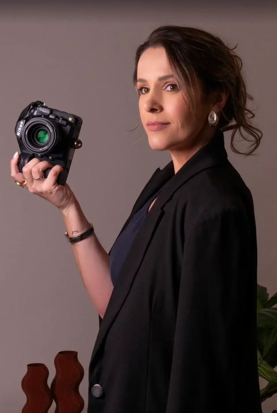 Tayze Apolinário Perini segurando a câmera, de blazer preto, no estúdio